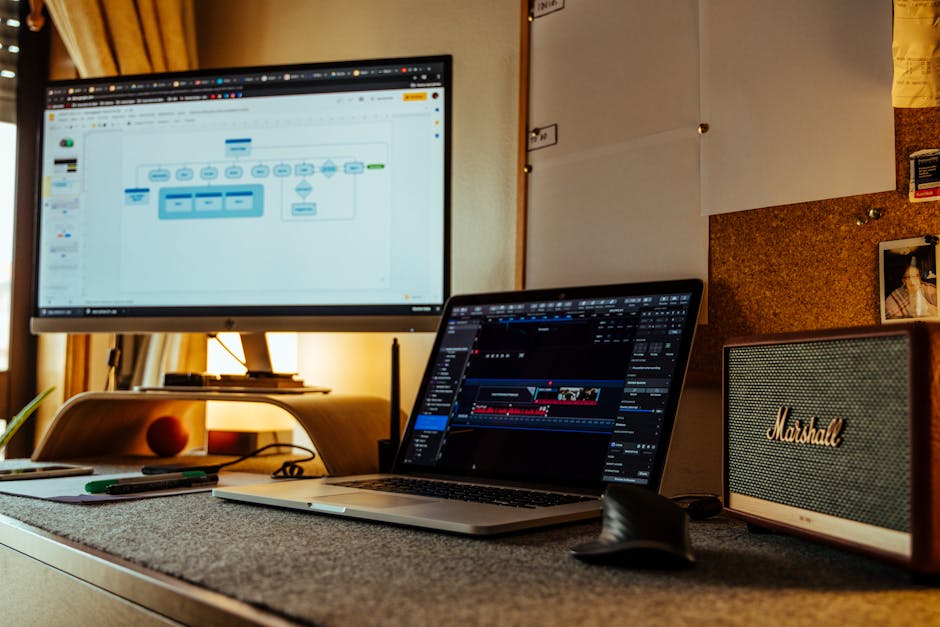 Cozy home office with laptop, large monitor, and speakers, ideal for productivity and digital work.